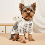 A small fluffy brown dog wearing a soft fuzzy sweater with a gray, white, and beige plaid pattern and white ribbed trim, posed indoors against a light neutral background.